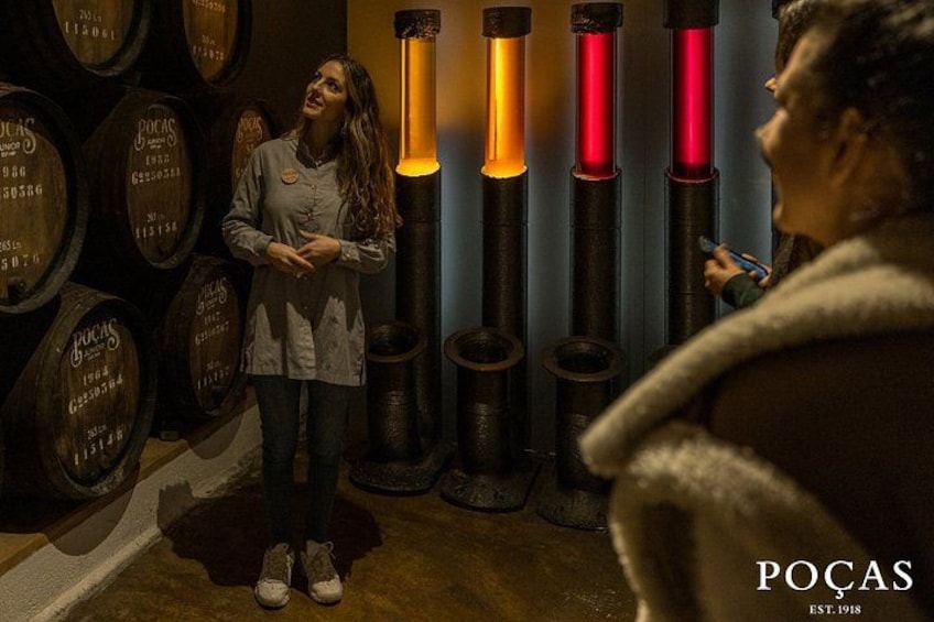 A person standing in front of wooden barrels with a sign that reads 'POCAS EST. 1918'. 3