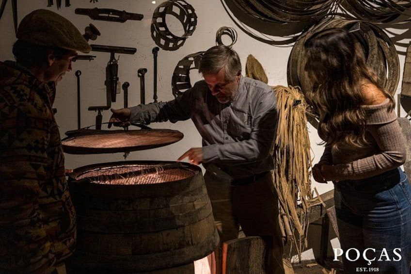 A person working with a large wooden barrel, another person observing, and a third person holding a rope. 2