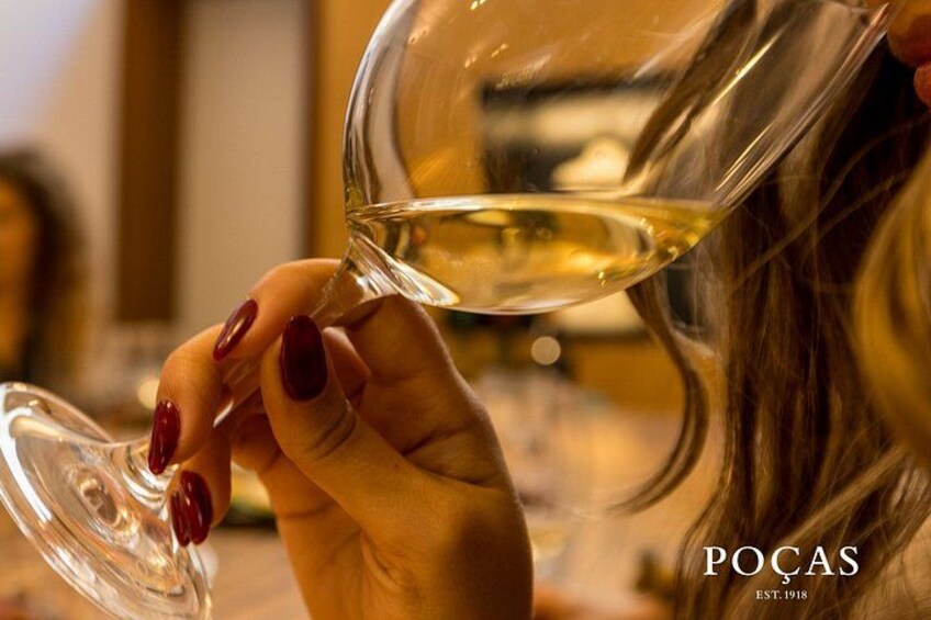 A person holding a wine glass with a clear liquid, presumably wine, with the brand 'POCAS' visible. 2
