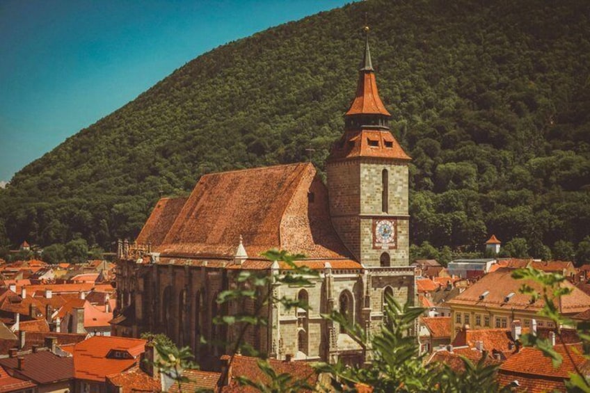 Una iglesia histórica con una torre del reloj, rodeada de edificios de tejados rojos y una colina boscosa al fondo. 2
