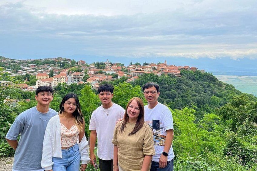 A group of people standing on a hill overlooking a coastal town with buildings and greenery. 2