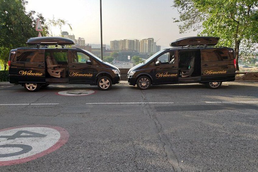 Two black vans with 'Welcome Armenia' written on the side parked on a road with a speed limit sign. 3