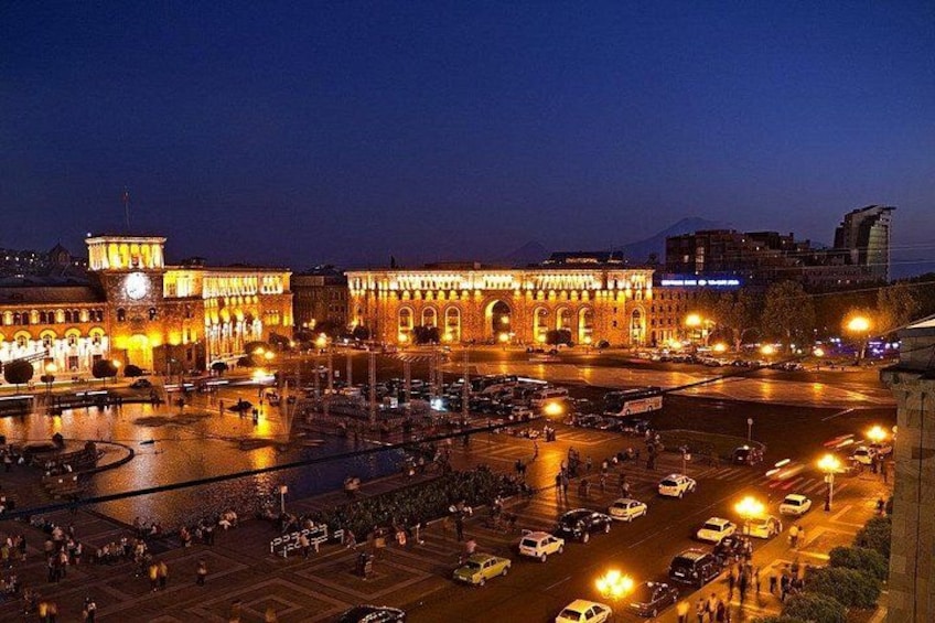 A well-lit historic building with a clock tower, surrounded by a busy intersection with cars and pedestrians. 4