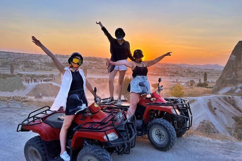 Tres personas en vehículos todo terreno con los brazos levantados al atardecer. 1