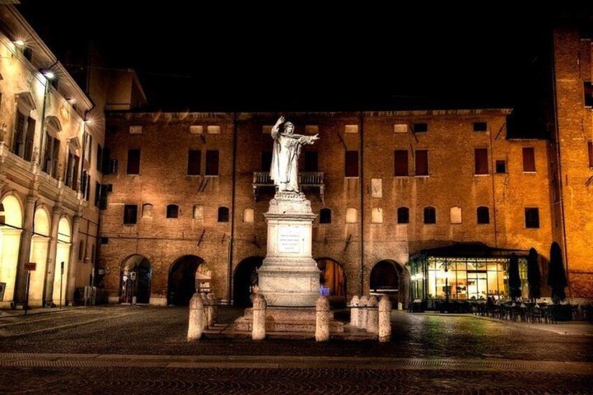 Une vue nocturne d’une place où se trouve une statue au centre, entourée de bâtiments historiques dotés de portes en arc de cercle. 5