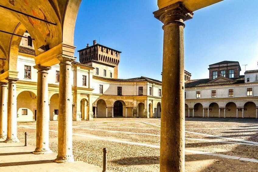 An open courtyard with arches, columns, and buildings in the background. 2