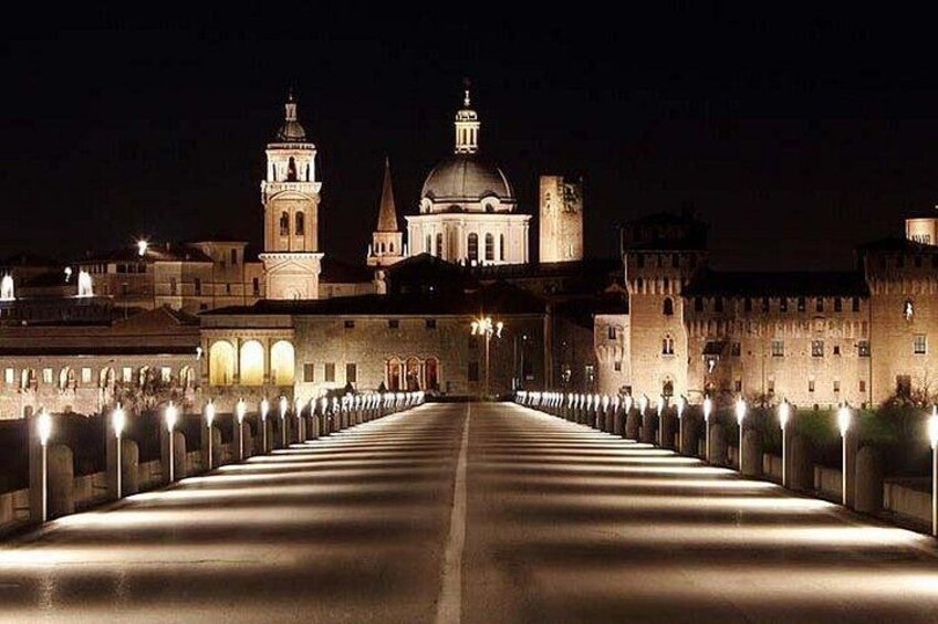 A long, illuminated bridge leading to a historic building with towers and domes. 2