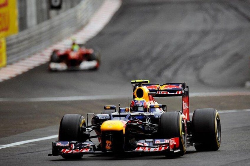 Een Formule 1 raceauto op een circuit, met een andere auto op de achtergrond. 3