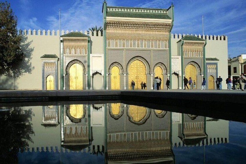 Un edificio histórico con amplias puertas arqueadas y detalles intrincados en cerámica, reflejado en el agua. 2