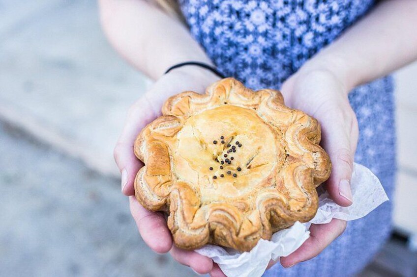A person holding a pastry with a crimped edge and a patterned top, possibly a savory pie or tart. 3