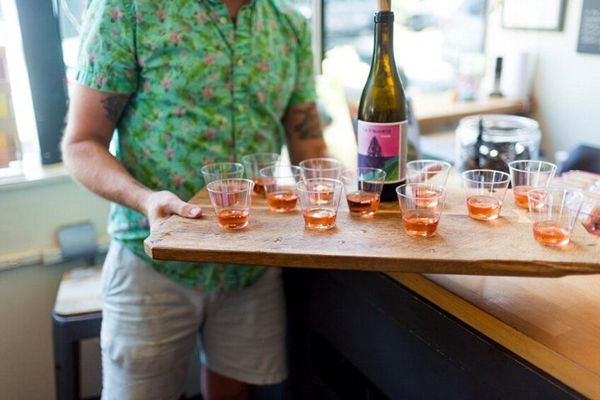 A person holding a tray with multiple shot glasses and a bottle of wine. 2