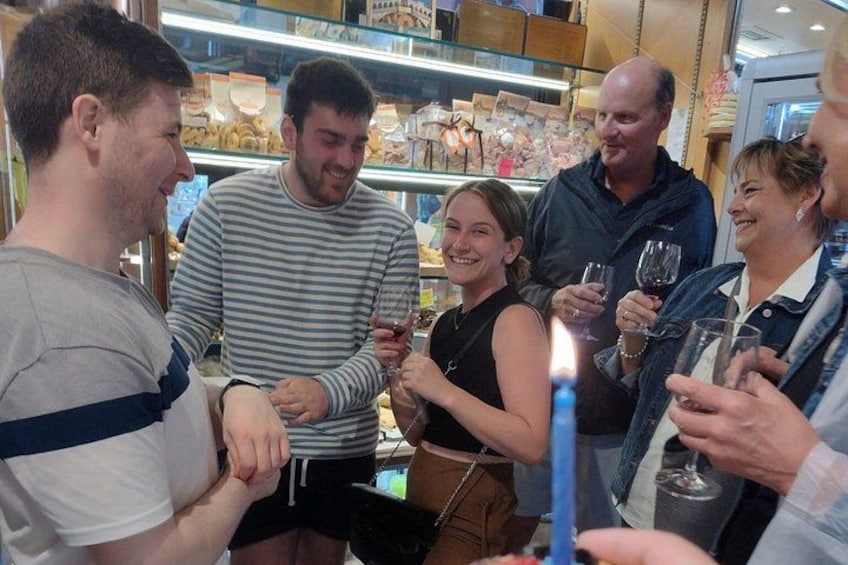 A group of people in a bakery, some holding glasses of wine. 5