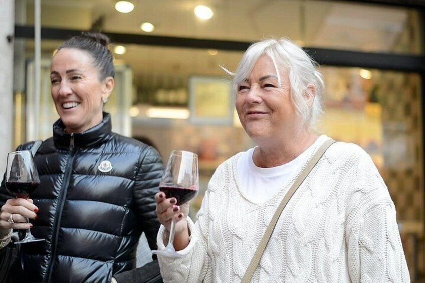 Two individuals holding wine glasses, standing in front of a building with glass doors. 4