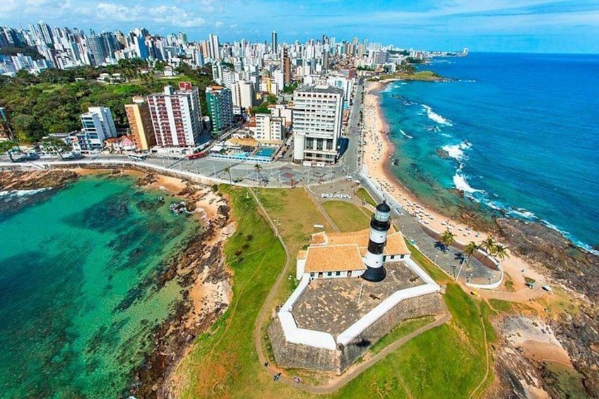 Un paisaje costero con un faro destacado, una playa y una zona urbana densa con rascacielos. 5
