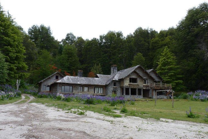 A rustic wooden house surrounded by a forested area with a gravel path leading to it. 5