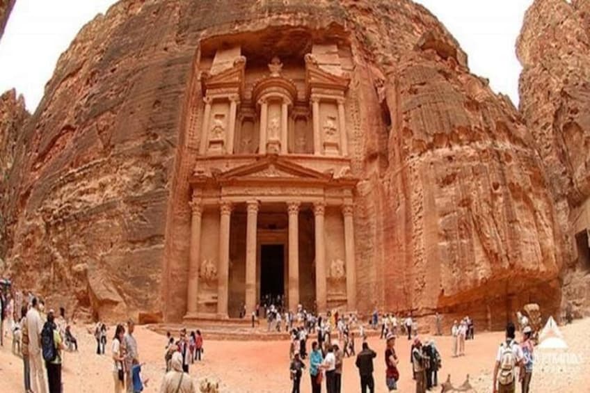 Un gran templo excavado en la roca, con columnas y un acceso central, rodeado de gente. 4