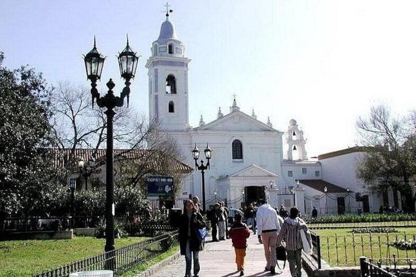Una iglesia blanca con un campanario, un sendero empedrado y algunas personas caminando. 2