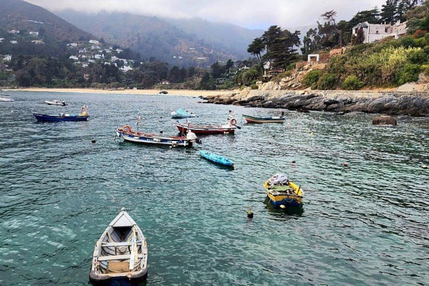 A coastal scene with boats anchored in clear water, a sandy beach, and a hilly landscape with buildings. 5