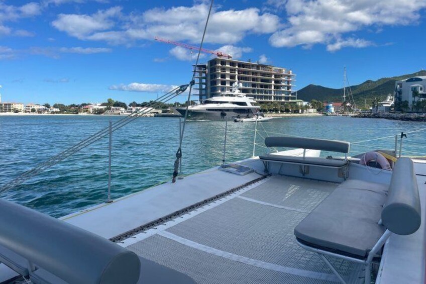 Cubierta de barco con vista a un puerto deportivo, un edificio grande y un paisaje montañoso al fondo. 2