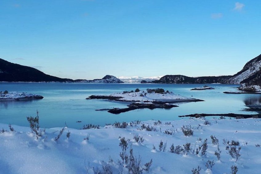 Een besneeerd landschap met een rustig meer, besneeuwde heuvels en schaarse begroeiing. 4