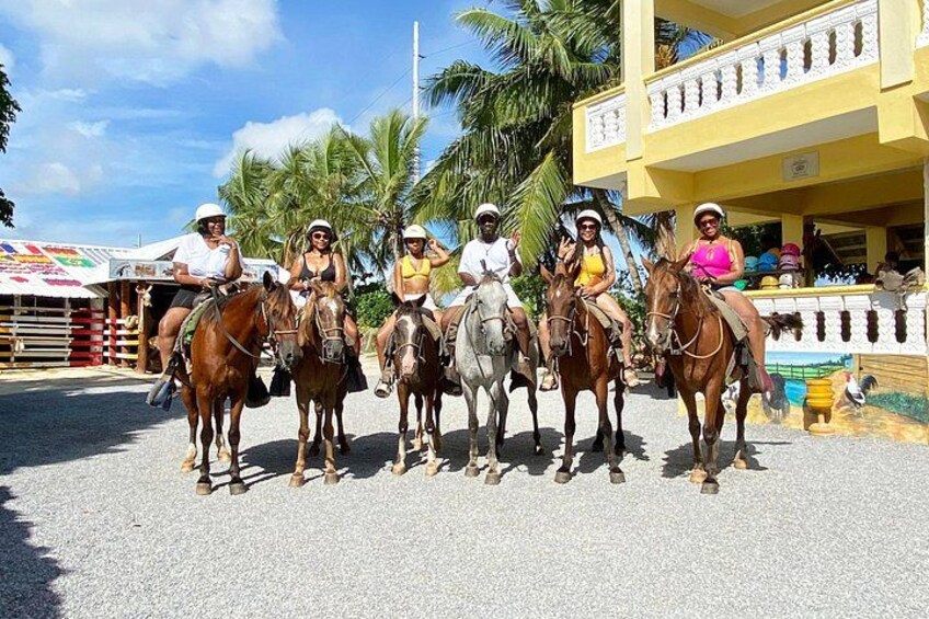A group of people riding horses in a stable area with a building in the background. 3