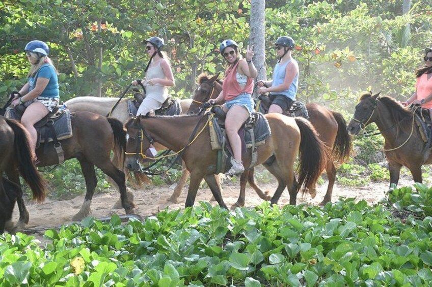 A group of people riding horses on a dirt path surrounded by greenery. 4