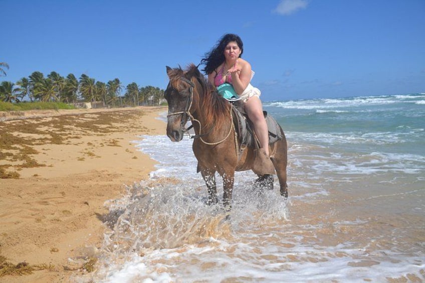 Una persona montando a caballo por una playa, con olas y palmeras al fondo. 2