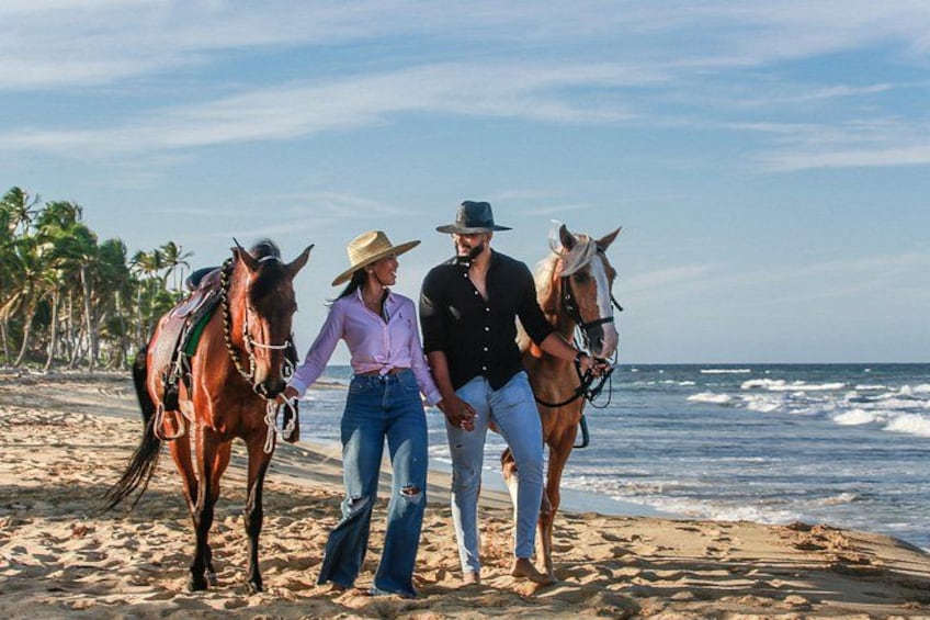 Una playa con dos caballos y dos personas caminando por la orilla. 4
