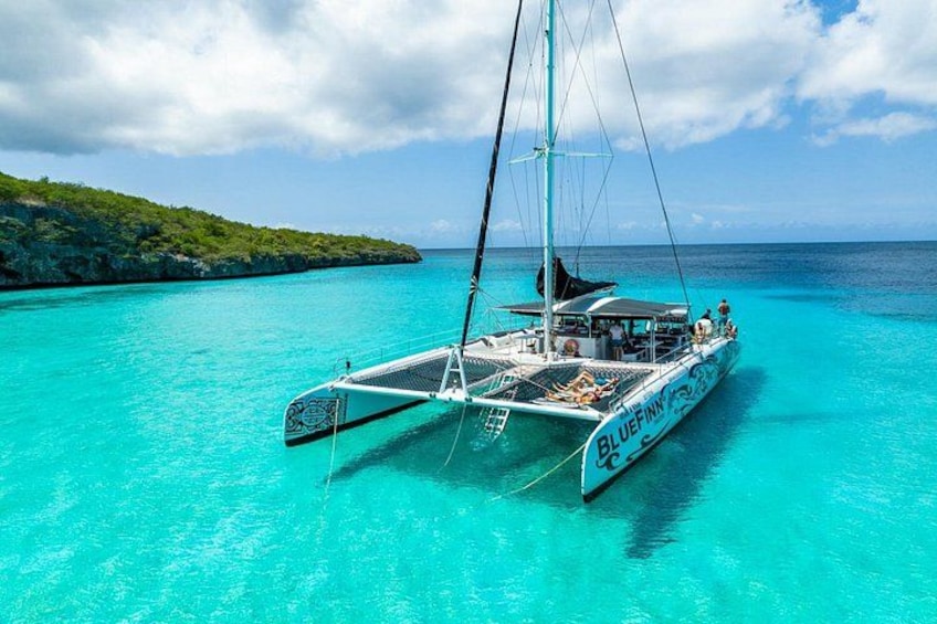 A sailboat named 'BLUEFINN' on turquoise waters with a rocky island in the background. 4
