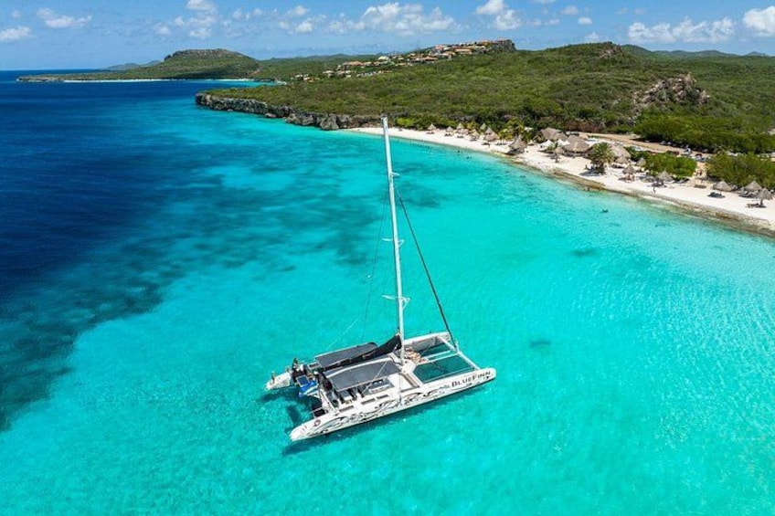 A sailboat on turquoise waters with a beach and greenery in the background. 5