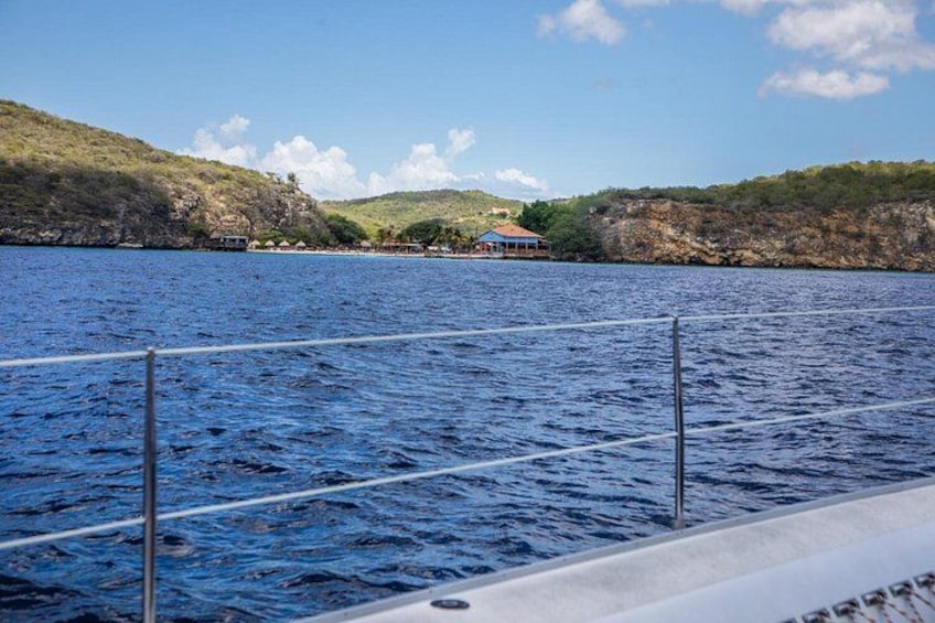 A calm body of water with a boat in the foreground and a house on a hill in the background. 2