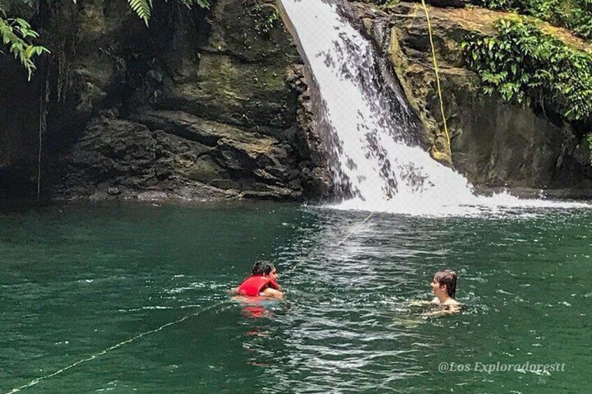 A waterfall in a natural setting with two people swimming in the water. 3