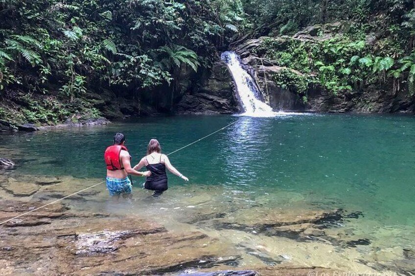 Two people standing in a clear river with a waterfall in the background. 2