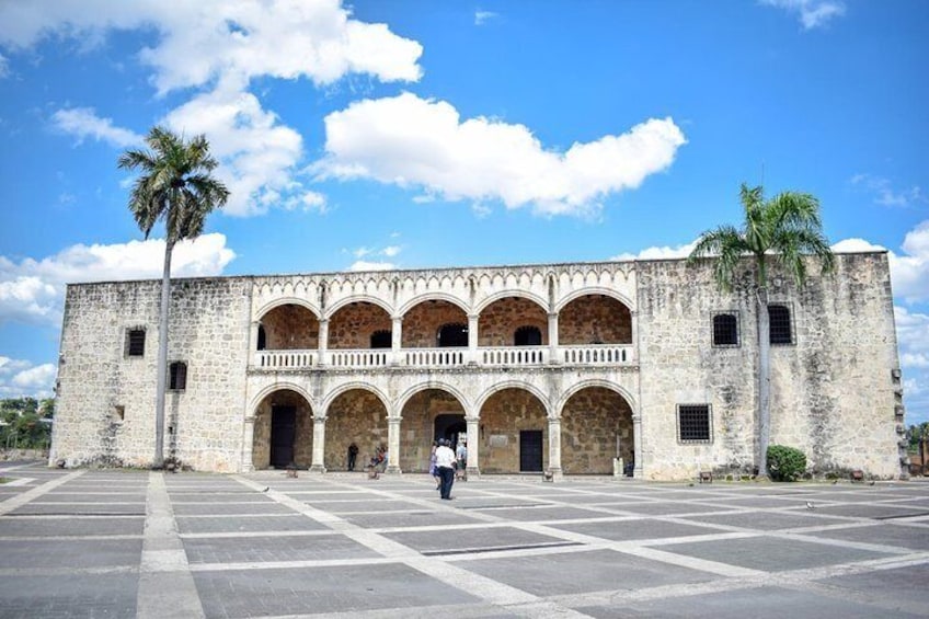 Un edificio histórico con un patio central, palmeras y un cielo despejado. 1
