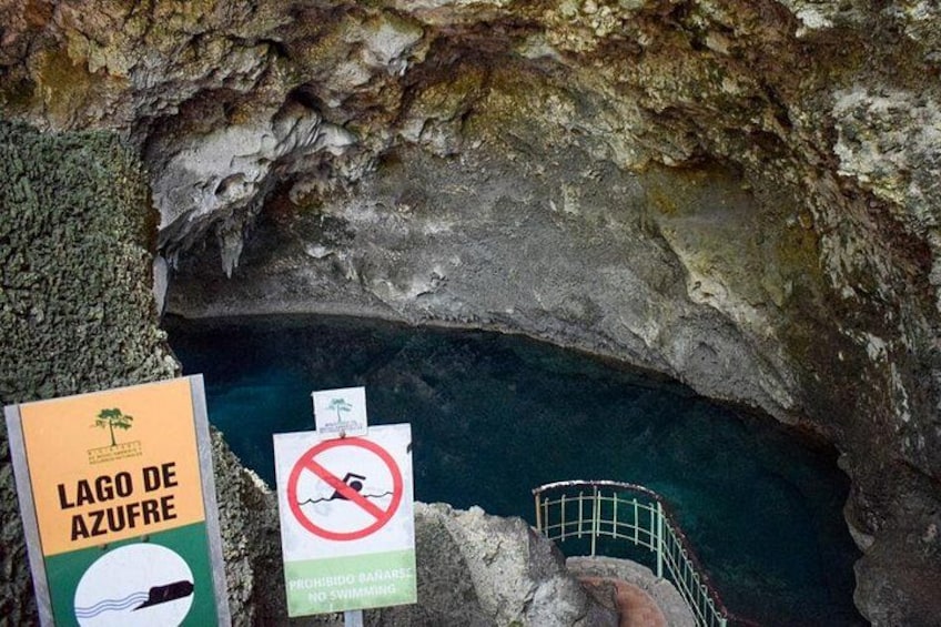 Entrada a una cueva con un cartel que indica 'Lago de Azufre' y una advertencia sobre la prohibición de bañarse. 4