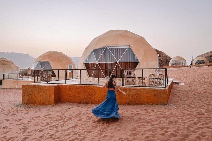 A desert landscape with large, dome-shaped structures and a person in a blue dress walking in the foreground. 1
