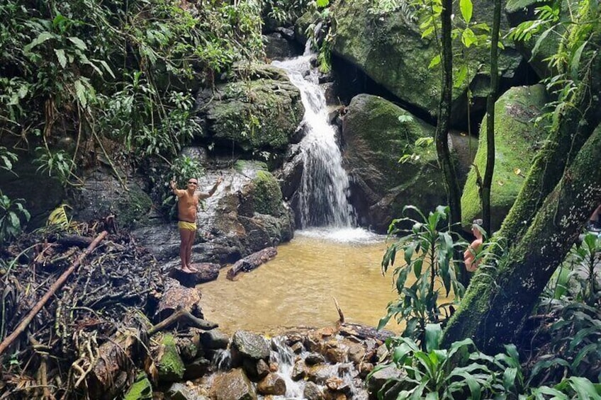 Una cascada en un área boscosa, con una persona de pie cerca del agua. 3