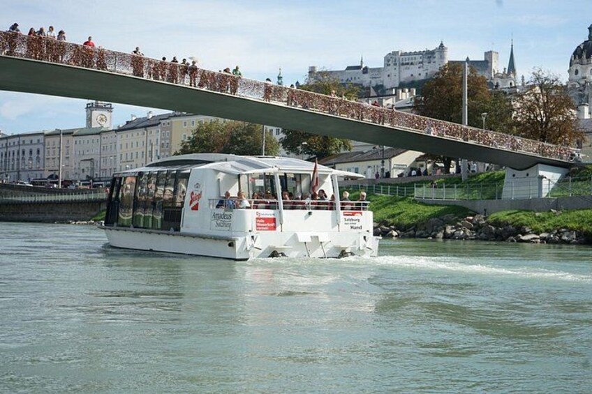 Een boot met passagiers op een rivier, een brug met mensen en gebouwen op de achtergrond. 3