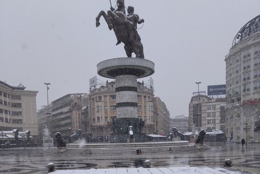 Una statua coperta di neve in una piazza, con edifici sullo sfondo. 1