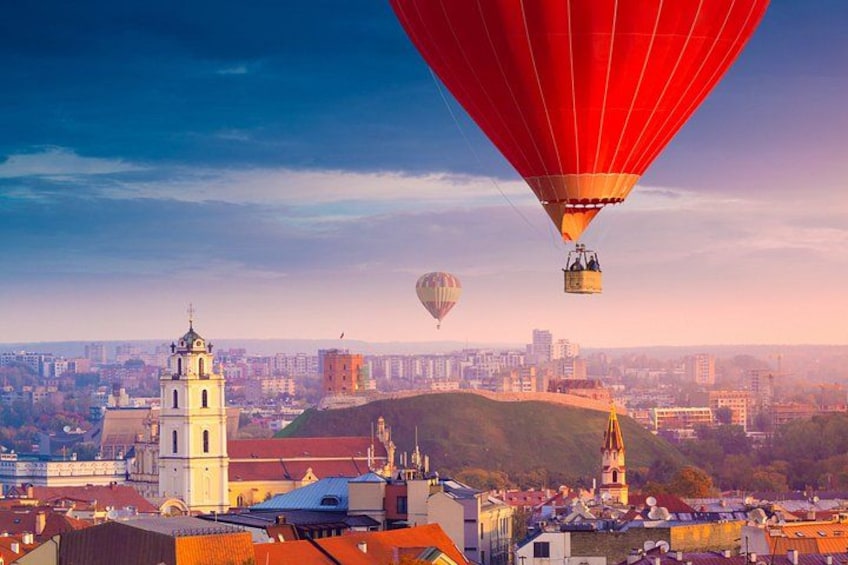 A cityscape with a prominent church, a hill, and hot air balloons. 1
