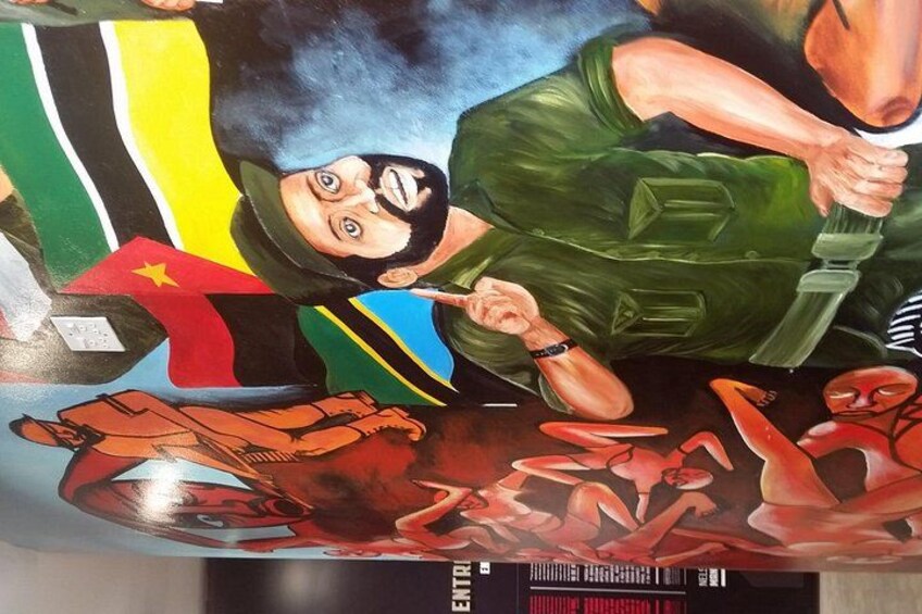 Un murale raffigura una persona in abiti militari che regge un'arma, circondata da varie bandiere e forme astratte. 2