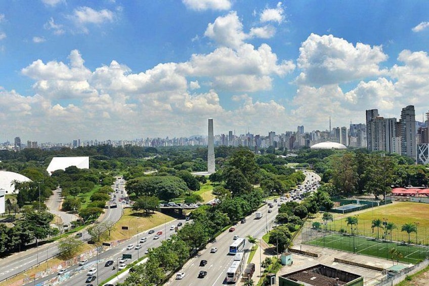 A cityscape with a prominent monument, a wide road, and a sports field. 5