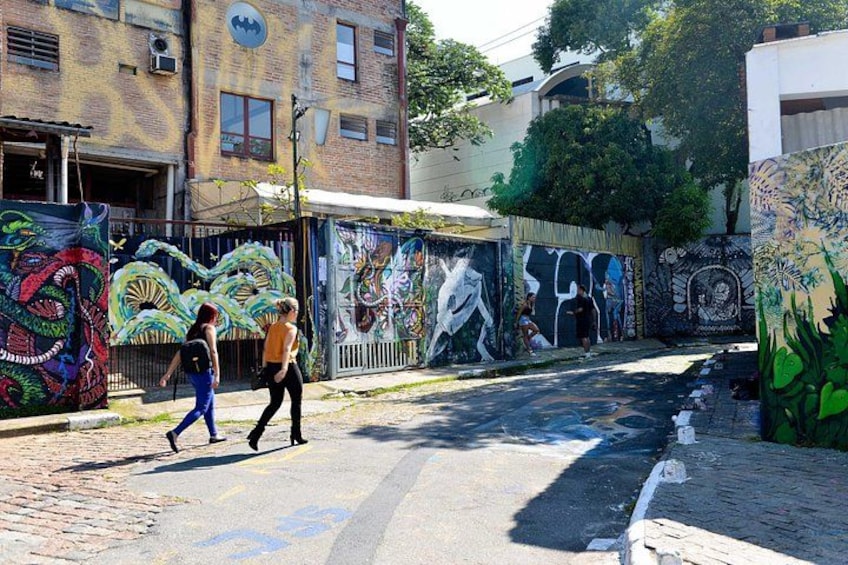 A street with graffiti-covered walls, a brick pavement, and buildings in the background. 3
