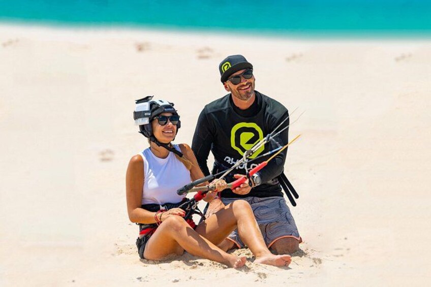 Dos personas sentadas en una playa arenosa, una sosteniendo una cometa. 1