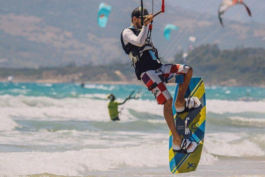 Una persona che pratica windsurf su una spiaggia con onde e altri windsurfer sullo sfondo. 2