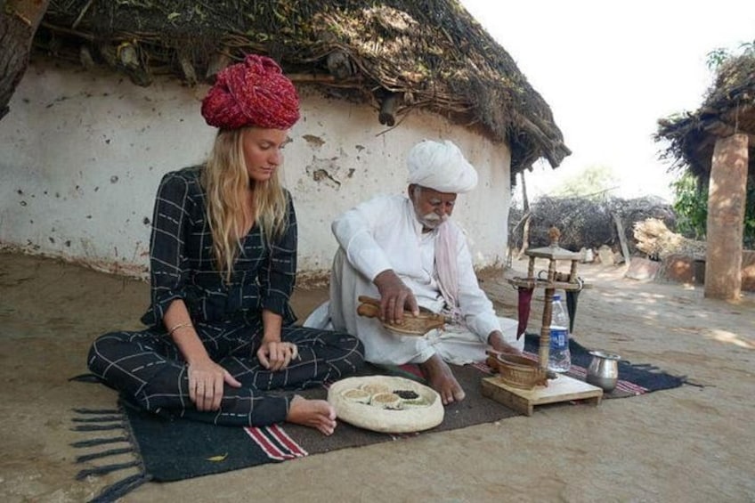 Two people sitting on a mat outdoors, one preparing food on a traditional stove. 1