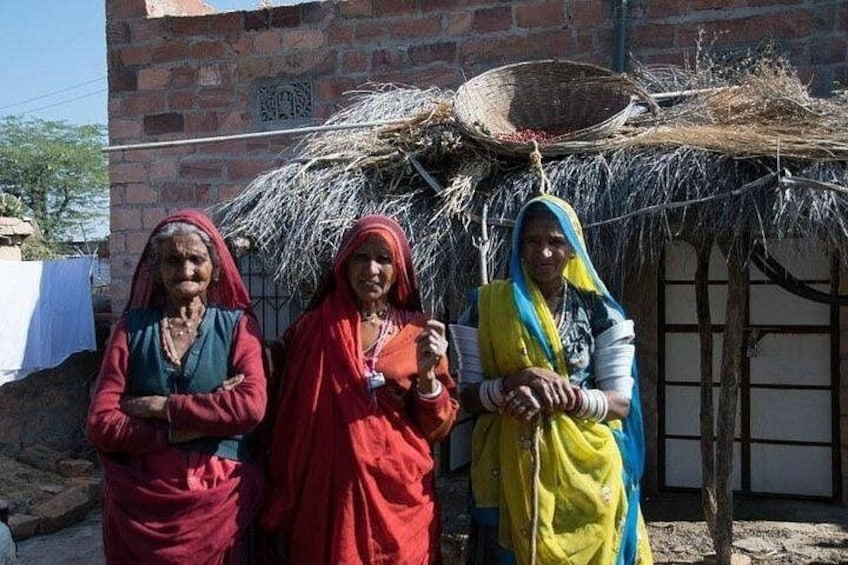 Three women standing in front of a thatched structure with a basket on top. 4