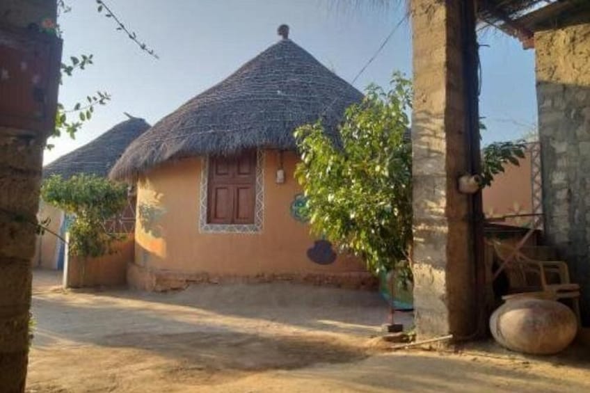 A traditional thatched-roof house with a wooden door, surrounded by a dirt yard and a stone wall. 3
