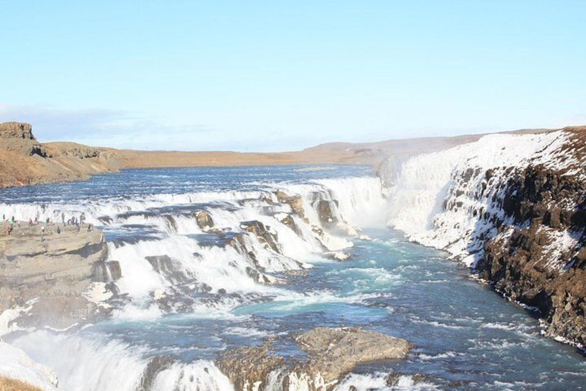 A waterfall cascading over rocky terrain with a clear sky above. 3