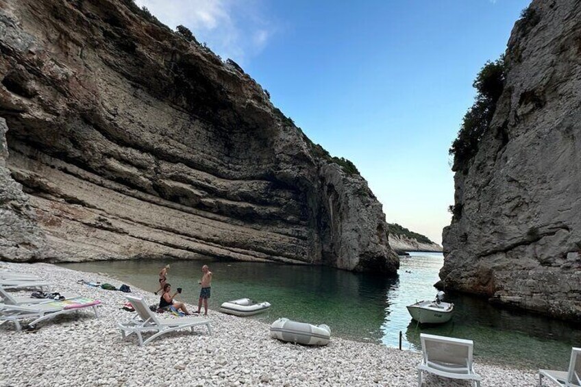 Una playa rocosa con agua cristalina, un bote y sillas de descanso. 5